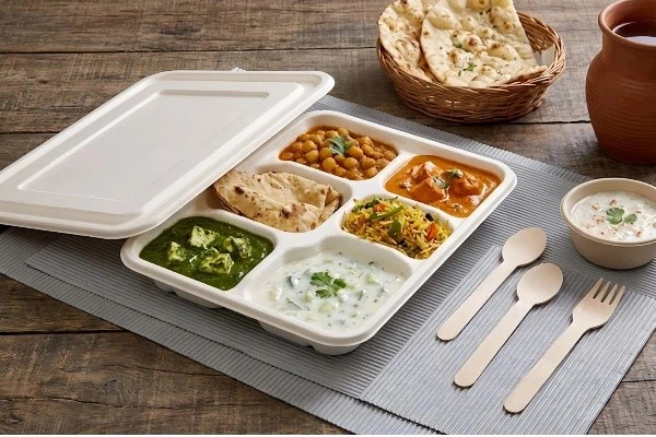 Biodegradable sugarcane trays served on a wooden restaurant table, featuring hot and cold foods Biodegradable sugarcane trays served on a wooden restaurant table, featuring hot and cold foods